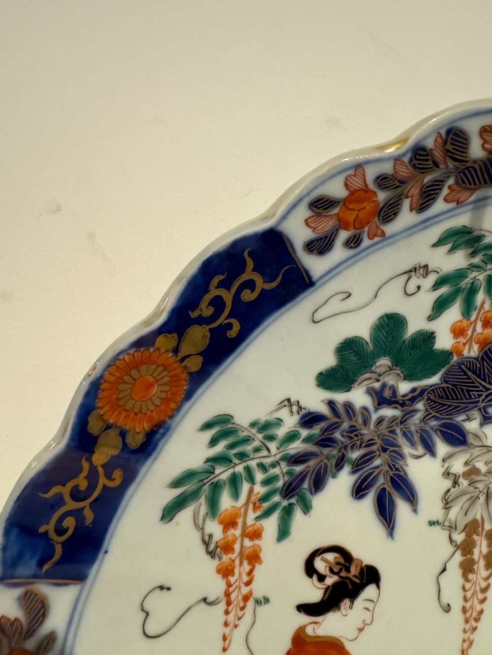 A large Japanese Meiji period porcelain charger plate with a scalloped edge, depicting women in traditional kimonos beneath a tree, bordered in cobalt blue and floral motifs. View IV