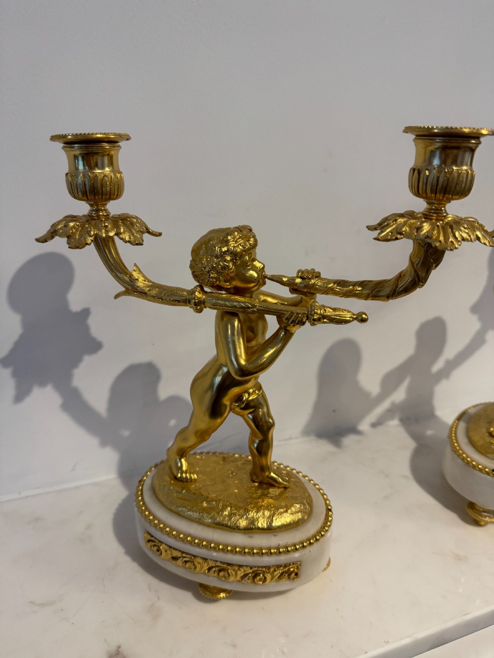 A pair of 19th-century French gilt bronze and white marble two-light candelabra featuring sculpted cherub figures supporting foliate candle branches. View IV