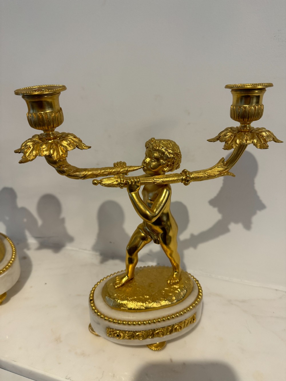 A pair of 19th-century French gilt bronze and white marble two-light candelabra featuring sculpted cherub figures supporting foliate candle branches. View V