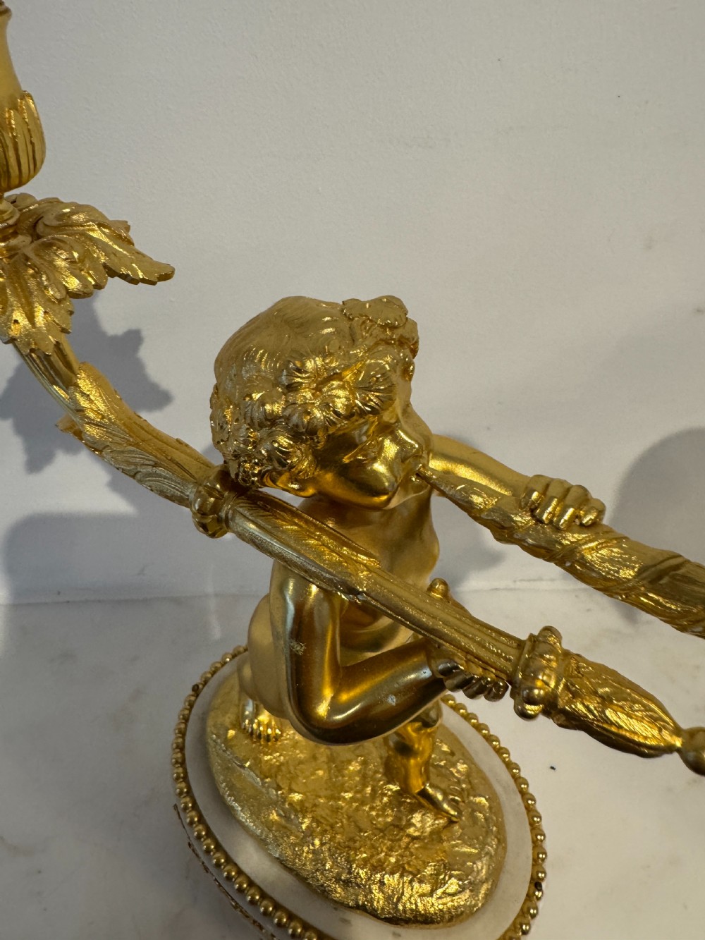 A pair of 19th-century French gilt bronze and white marble two-light candelabra featuring sculpted cherub figures supporting foliate candle branches. View VI