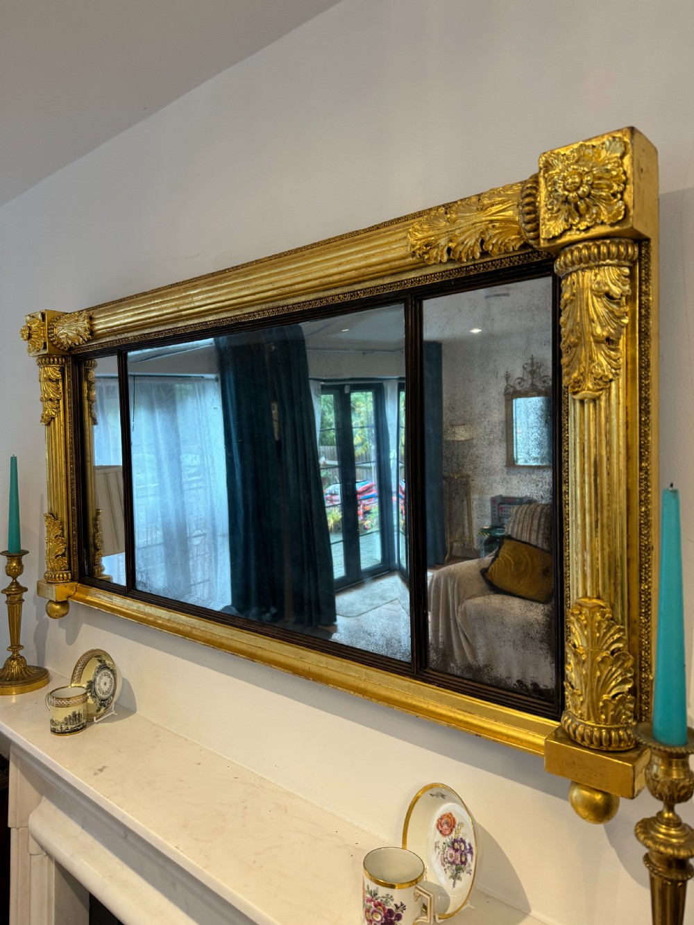 A wide Regency giltwood tripartite overmantel mirror featuring side fluted columns and carved leaf accents.