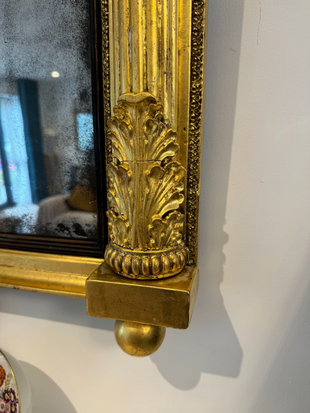 A wide Regency giltwood tripartite overmantel mirror featuring side fluted columns and carved leaf accents. View IV