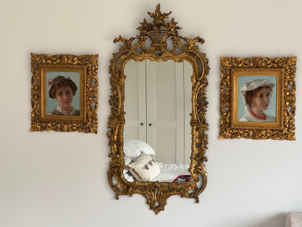 An oil portrait depicting a young child in traditional costume wearing a red coral necklace, presented inside an ornate carved giltwood frame. View IV