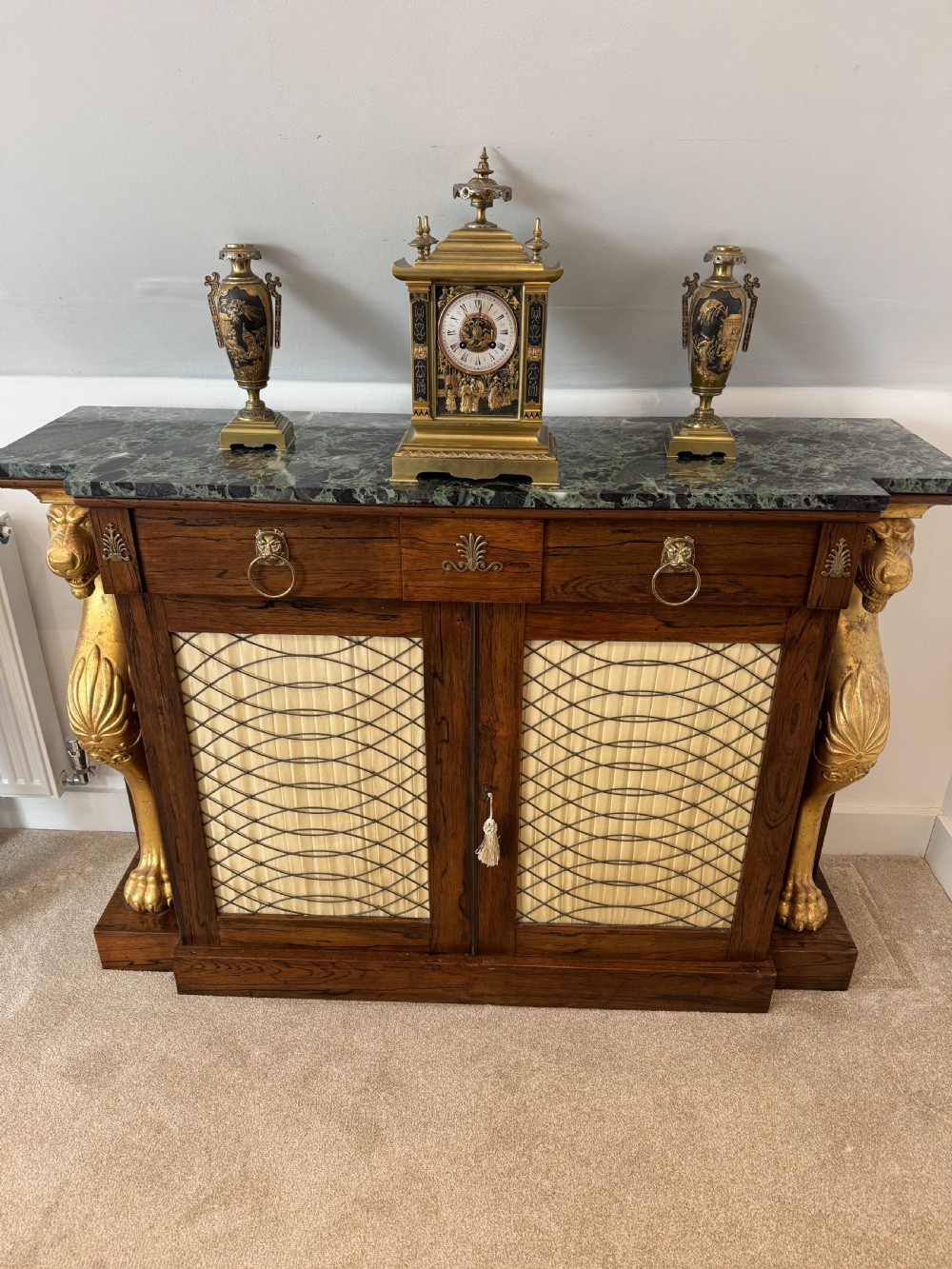 A Regency rosewood side cabinet featuring a dark green marble top, gilt lion monopodia legs, and two brass grille doors lined with pleated fabric. View III