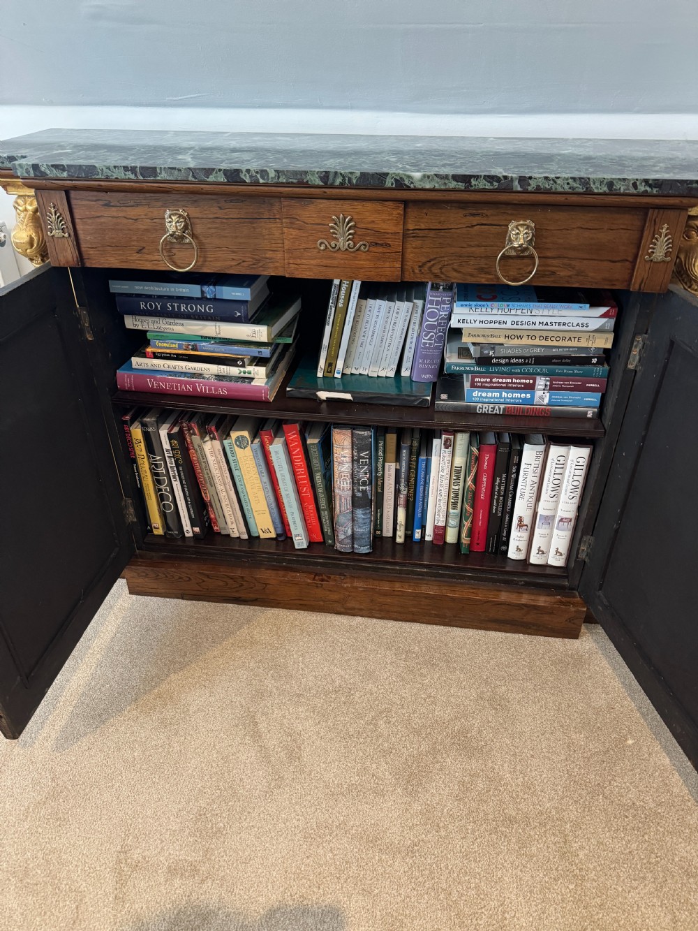 A Regency rosewood side cabinet featuring a dark green marble top, gilt lion monopodia legs, and two brass grille doors lined with pleated fabric. View V