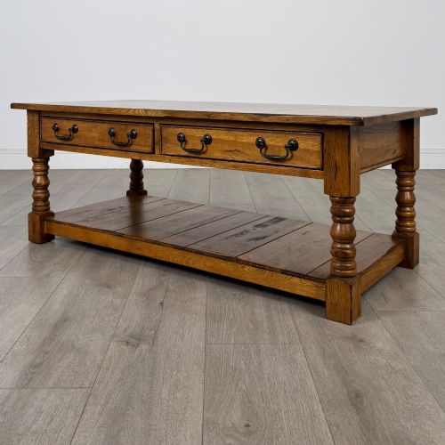 fig 1. A low rectangular oak coffee table featuring two drawers with metal drop handles, turned legs, and an open lower plank shelf.