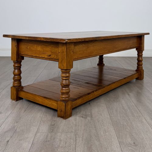 fig 3. A low rectangular oak coffee table featuring two drawers with metal drop handles, turned legs, and an open lower plank shelf.