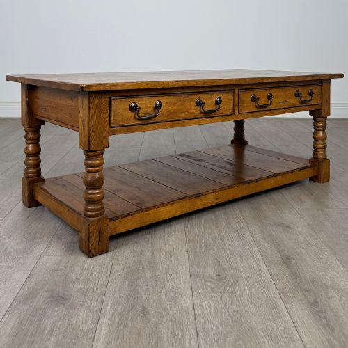 fig 7. A low rectangular oak coffee table featuring two drawers with metal drop handles, turned legs, and an open lower plank shelf.