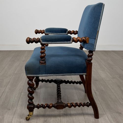 fig 1. A nineteenth-century dark oak armchair featuring barley twist legs and stretchers, blue fabric upholstery, and brass front castors.