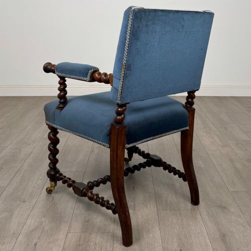 fig 2. A nineteenth-century dark oak armchair featuring barley twist legs and stretchers, blue fabric upholstery, and brass front castors.