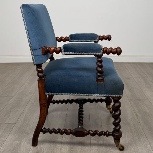 fig 5. A nineteenth-century dark oak armchair featuring barley twist legs and stretchers, blue fabric upholstery, and brass front castors.