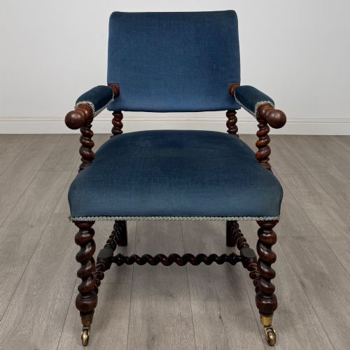 fig 7. A nineteenth-century dark oak armchair featuring barley twist legs and stretchers, blue fabric upholstery, and brass front castors.