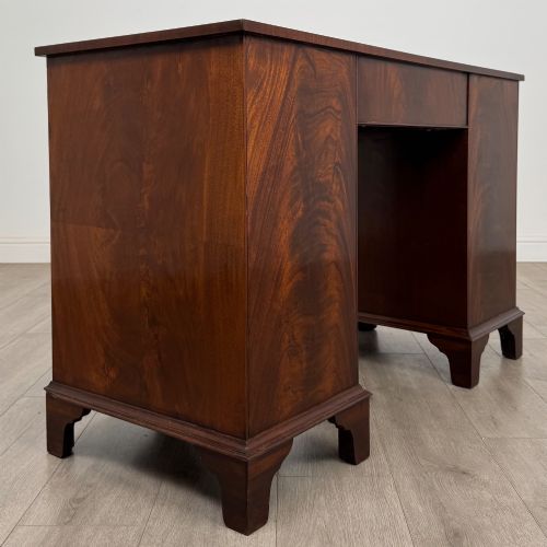 fig 3. A twentieth-century mahogany kneehole desk featuring a serpentine front, multiple drawers with brass swan-neck handles, and bracket feet.