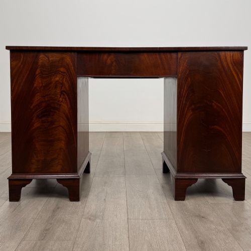 fig 4. A twentieth-century mahogany kneehole desk featuring a serpentine front, multiple drawers with brass swan-neck handles, and bracket feet.