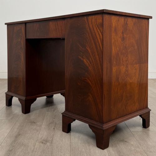 fig 5. A twentieth-century mahogany kneehole desk featuring a serpentine front, multiple drawers with brass swan-neck handles, and bracket feet.