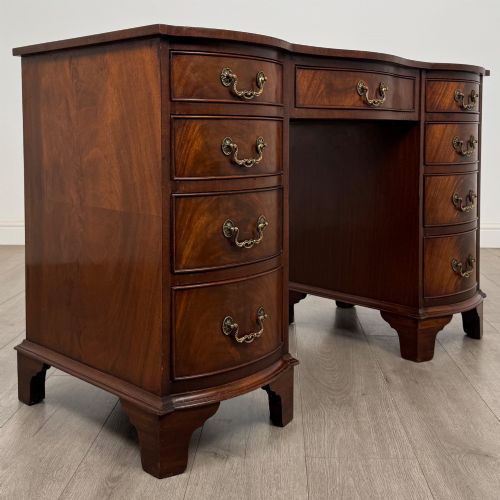 fig 7. A twentieth-century mahogany kneehole desk featuring a serpentine front, multiple drawers with brass swan-neck handles, and bracket feet.