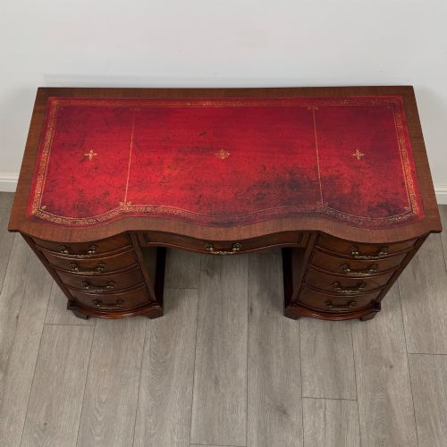 fig 8. A twentieth-century mahogany kneehole desk featuring a serpentine front, multiple drawers with brass swan-neck handles, and bracket feet.