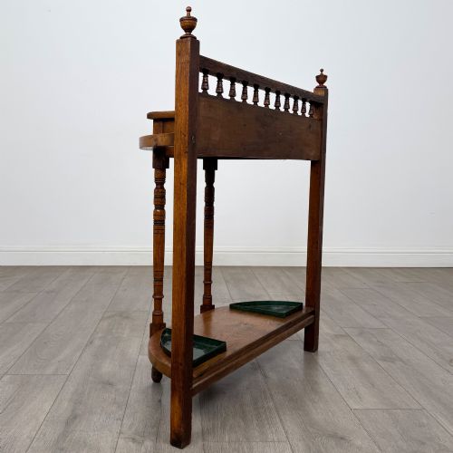 fig 3. An Edwardian golden oak hall stand with a top spindle gallery, central glove drawer with brass handle, twin umbrella rail apertures, and metal drip trays on the lower shelf.