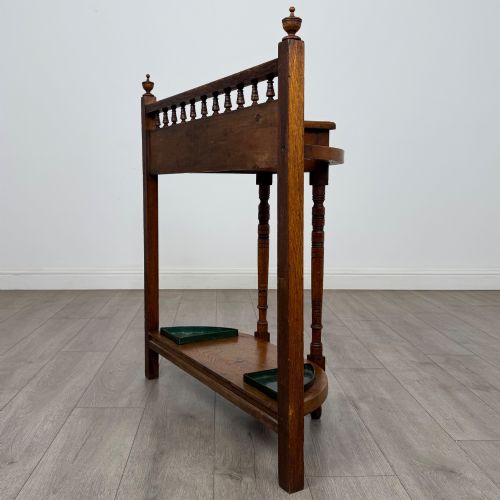 fig 5. An Edwardian golden oak hall stand with a top spindle gallery, central glove drawer with brass handle, twin umbrella rail apertures, and metal drip trays on the lower shelf.