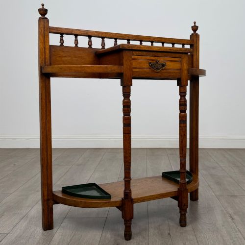 fig 7. An Edwardian golden oak hall stand with a top spindle gallery, central glove drawer with brass handle, twin umbrella rail apertures, and metal drip trays on the lower shelf.