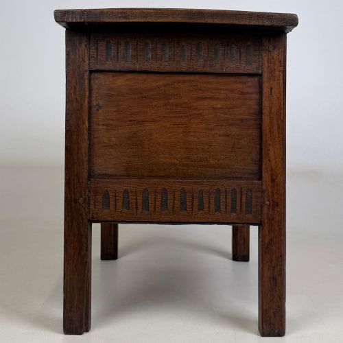 fig 6. An 18th-century small oak coffer chest featuring carved vertical fluting along the top and bottom rails, a central decorative brass escutcheon, and straight squared legs.