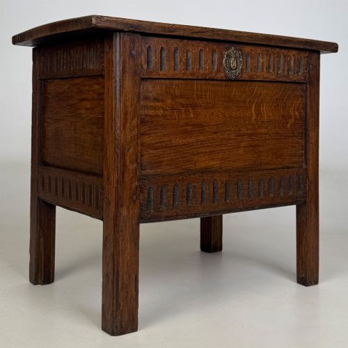 fig 7. An 18th-century small oak coffer chest featuring carved vertical fluting along the top and bottom rails, a central decorative brass escutcheon, and straight squared legs.