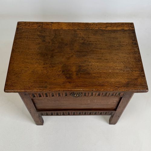 fig 8. An 18th-century small oak coffer chest featuring carved vertical fluting along the top and bottom rails, a central decorative brass escutcheon, and straight squared legs.