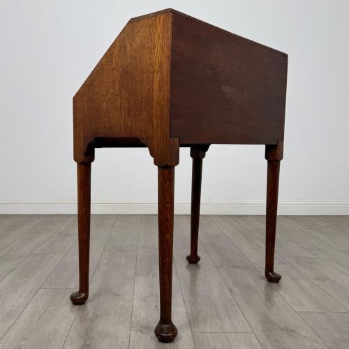 fig 4. A golden oak slant-front writing bureau standing on four slender legs with pad feet, featuring a single lower drawer with drop handles and a hinged writing slope.