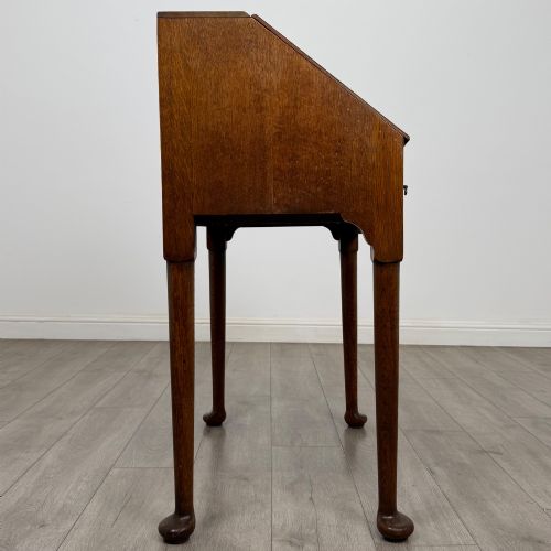 fig 7. A golden oak slant-front writing bureau standing on four slender legs with pad feet, featuring a single lower drawer with drop handles and a hinged writing slope.