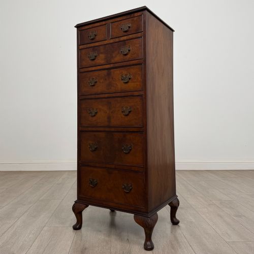fig 1. A tall, narrow dark brown burr walnut chest of drawers featuring brass handles and carved cabriole legs.