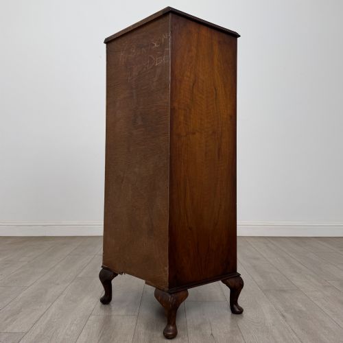 fig 5. A tall, narrow dark brown burr walnut chest of drawers featuring brass handles and carved cabriole legs.