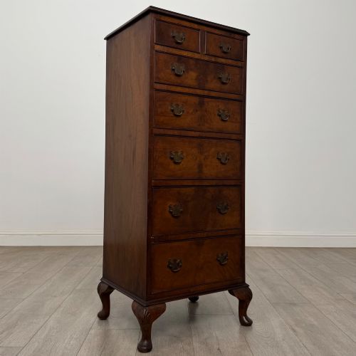 fig 7. A tall, narrow dark brown burr walnut chest of drawers featuring brass handles and carved cabriole legs.