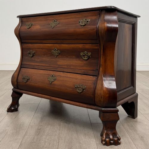 fig 1. A small 20th-century Dutch bombe chest of drawers made from polished brown wood with three drawers, brass handles, and carved claw feet.