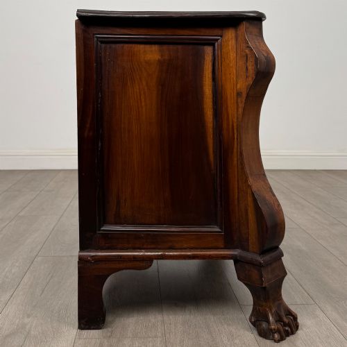 fig 6. A small 20th-century Dutch bombe chest of drawers made from polished brown wood with three drawers, brass handles, and carved claw feet.
