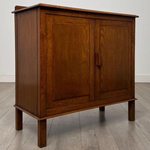 fig 8. An Edwardian warm brown oak fitted cupboard featuring twin recessed panel doors, a central wooden latch, and four straight legs.