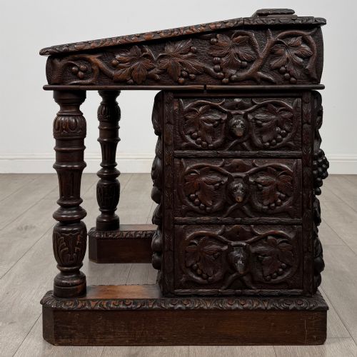 fig 2. A 19th-century Victorian carved oak davenport desk featuring heavy foliate carvings, turned columns, and a green leather insert.