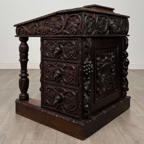 fig 3. A 19th-century Victorian carved oak davenport desk featuring heavy foliate carvings, turned columns, and a green leather insert.