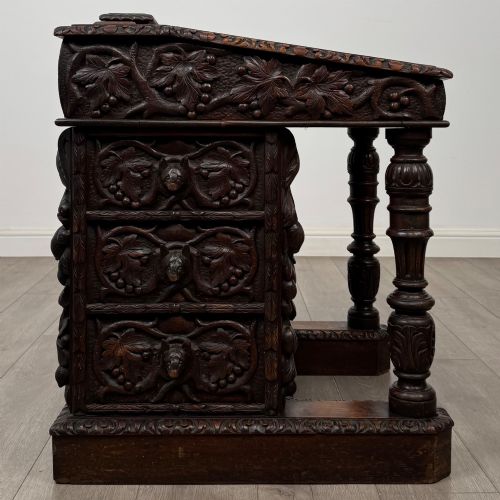fig 6. A 19th-century Victorian carved oak davenport desk featuring heavy foliate carvings, turned columns, and a green leather insert.