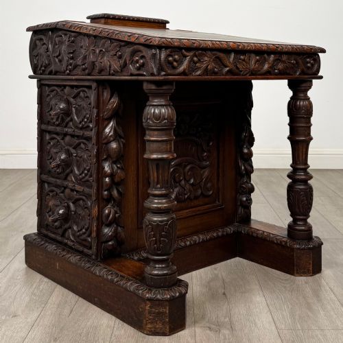 fig 7. A 19th-century Victorian carved oak davenport desk featuring heavy foliate carvings, turned columns, and a green leather insert.