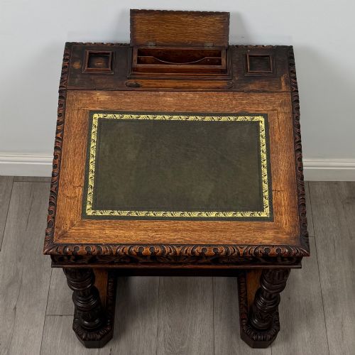 fig 8. A 19th-century Victorian carved oak davenport desk featuring heavy foliate carvings, turned columns, and a green leather insert.