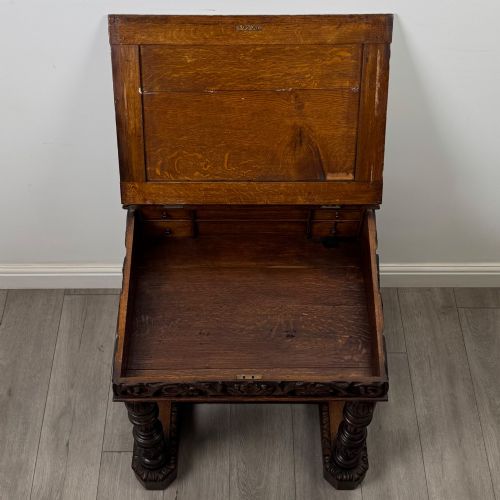 fig 9. A 19th-century Victorian carved oak davenport desk featuring heavy foliate carvings, turned columns, and a green leather insert.