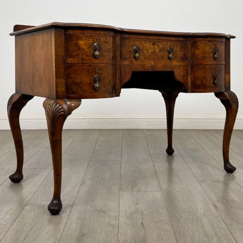 fig 7. An Edwardian burr walnut writing table featuring five drawers with brass drop handles and carved cabriole legs.