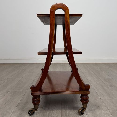 fig 1. A three-tiered mahogany trolley featuring arched reeded side supports and turned feet resting on brass castors.