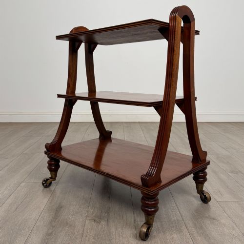 fig 4. A three-tiered mahogany trolley featuring arched reeded side supports and turned feet resting on brass castors.