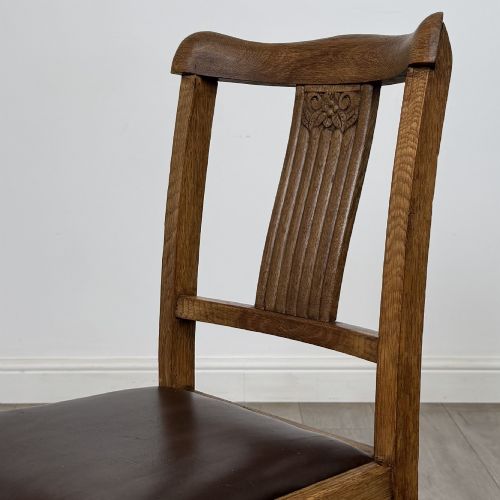 fig 4. An early twentieth-century oak dining table featuring carved frieze detailing and heavy turned legs, shown alongside four matching oak dining chairs with dark leather seats.