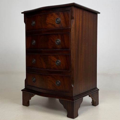 fig 1. A small mahogany chest of four drawers featuring flame grain veneer fronts, circular brass ring handles, and bracket feet.