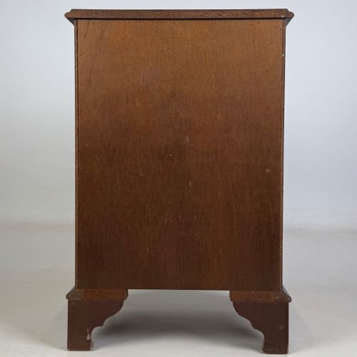 fig 4. A small mahogany chest of four drawers featuring flame grain veneer fronts, circular brass ring handles, and bracket feet.