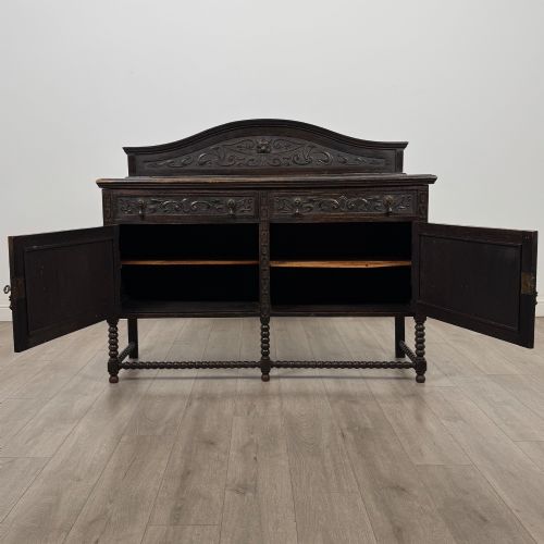fig 1. A dark oak 19th-century sideboard featuring carved lion mask motifs, scrollwork panel doors, and bobbin-turned legs connected by stretchers.