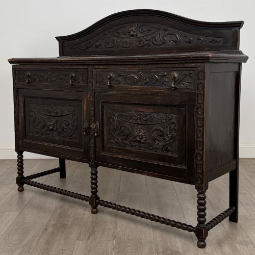 fig 2. A dark oak 19th-century sideboard featuring carved lion mask motifs, scrollwork panel doors, and bobbin-turned legs connected by stretchers.