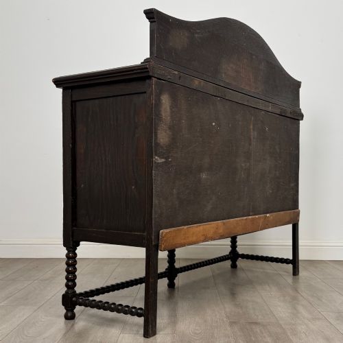 fig 4. A dark oak 19th-century sideboard featuring carved lion mask motifs, scrollwork panel doors, and bobbin-turned legs connected by stretchers.
